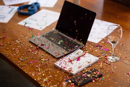 Workplace holiday events symbolized by confetti and a wine class on a desk with a laptop