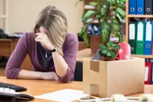 A wrongfully terminated employee sadly sitting at their desk with their personal belongings in a cardboard box.