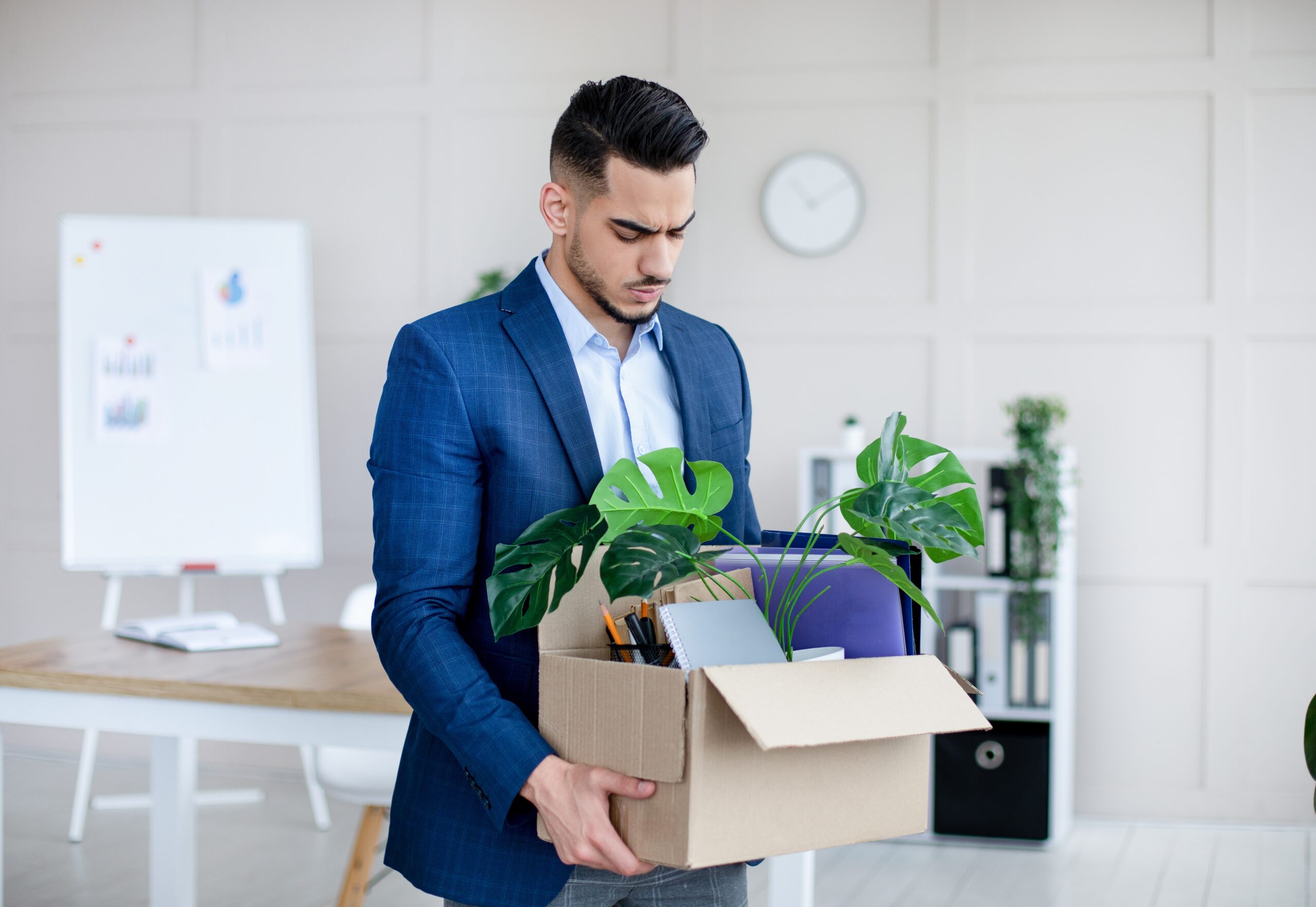 Male employee holds a box of office items after being wrongfully terminated.